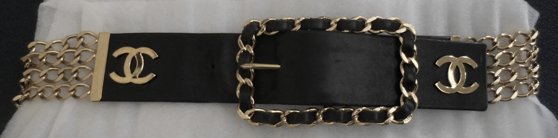 Black leather belt with gold chain and logo.